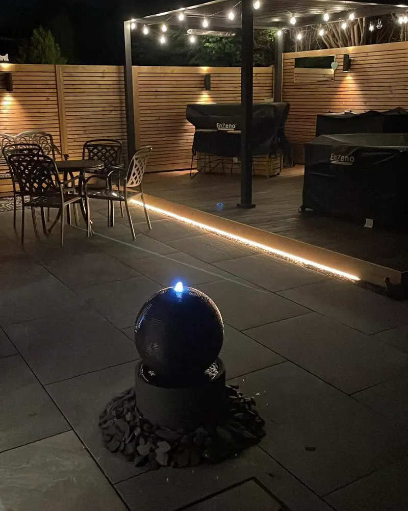 Pergola with festoon lighting and glowing LED strip along slatted fence at night