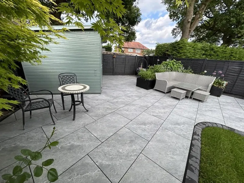 Grey porcelain patio with curved edging beside sage green garden building