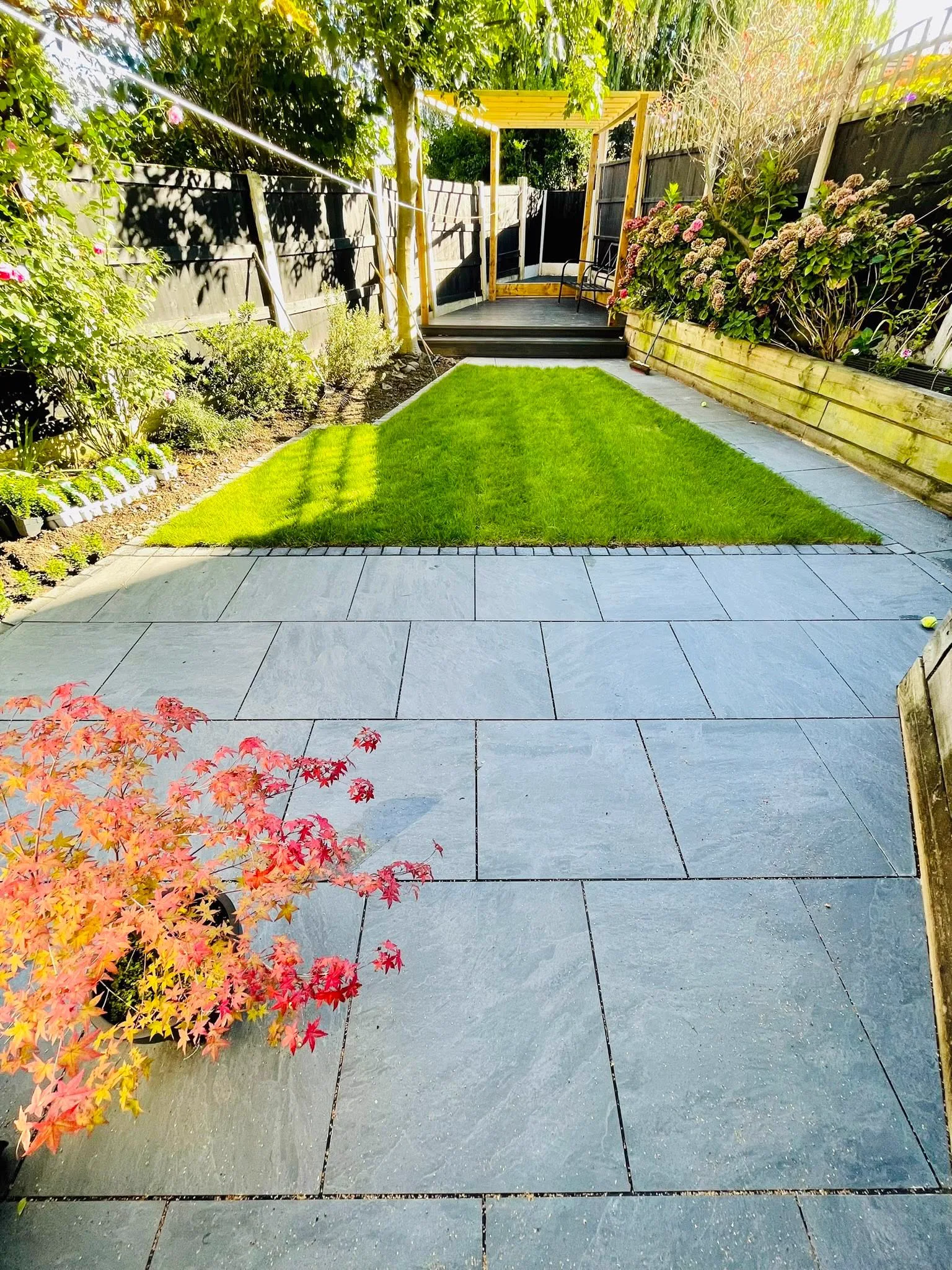 Slate-toned porcelain patio bordered by fresh lawn and timber pergola
