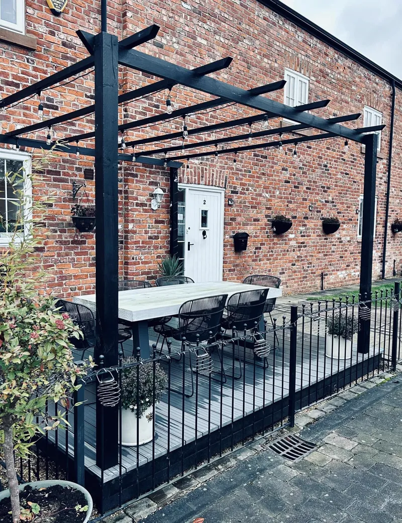 Black timber pergola with festoon lights over grey composite decking at a barn conversion